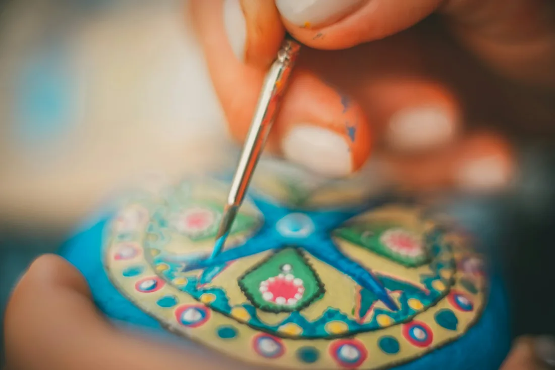Mano sujetando un pincel fino mientras pinta un motivo ornamental sobre una pieza lacada